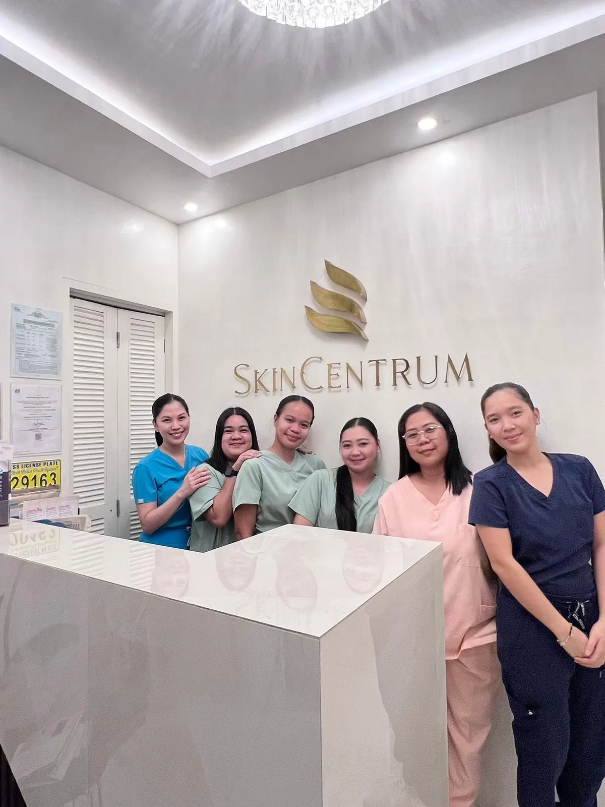 The SkinCentrum team behind the front desk with the gold SkinCentrum logo on the wall